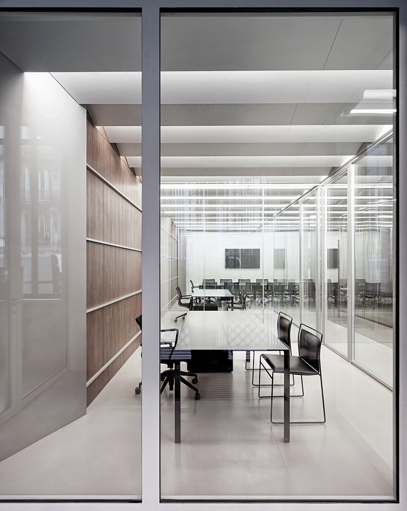Through floor-to-ceiling glass: meeting room interior with walnut wall, open shelving, black furniture