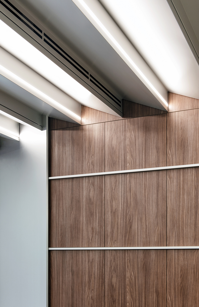 Wall junction: walnut timber panels meeting white ceiling baffles, aluminium trim at the edge