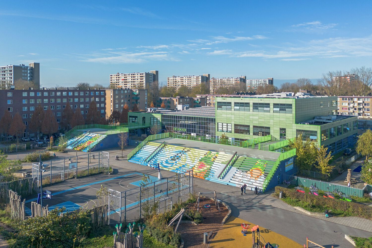 Elevated view showing the terraced seating leading to the paneled facade with a playground in the foreground