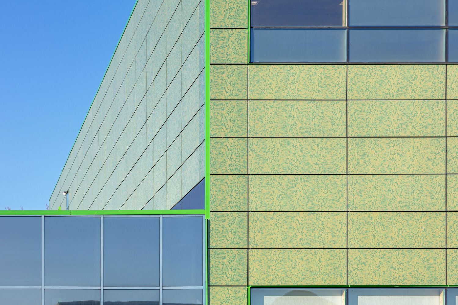 Corner detail of the facade showing green panel joints and window mullions against a clear sky