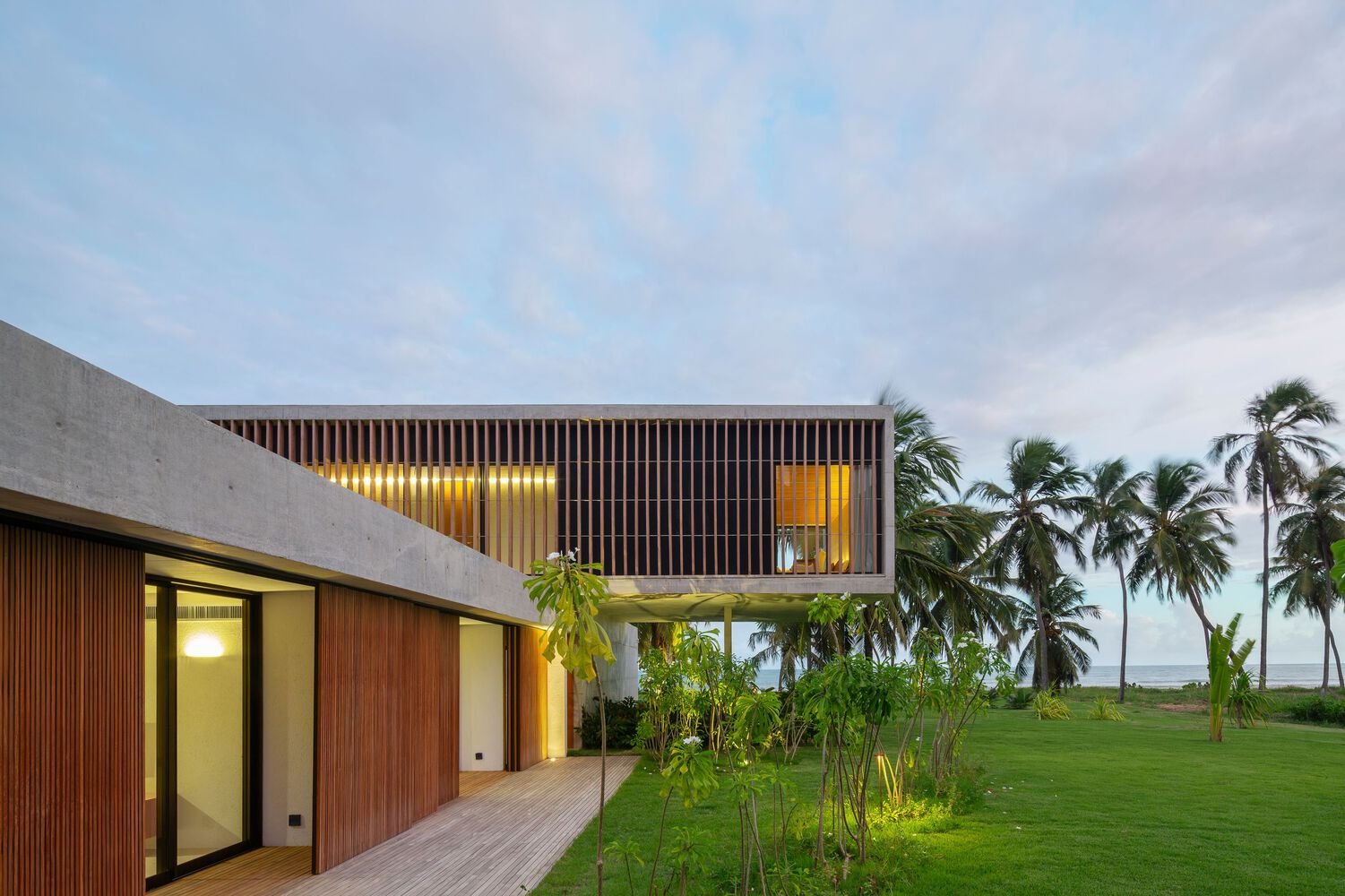 Dusk: the two volumes glowing, concrete base lit warmly, timber screen catching the last light