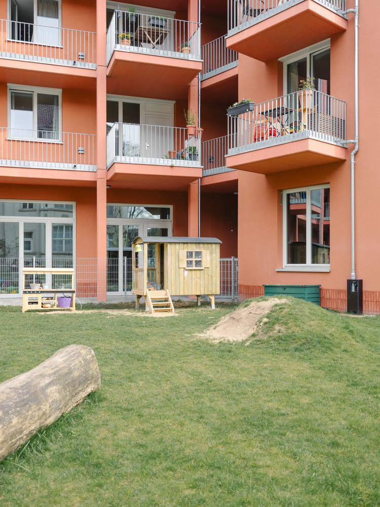 Coral-colored facade with recessed balconies above a shared lawn with a small wooden playhouse