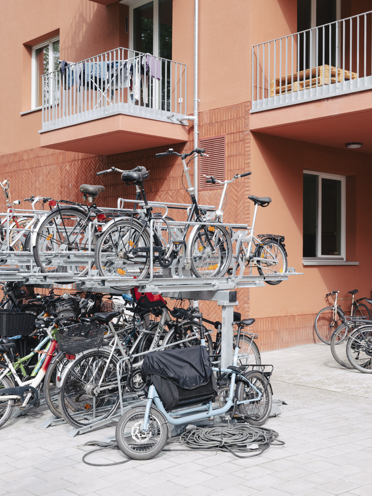 Two-tier bicycle parking racks filled with bikes beneath residential balconies with white railings