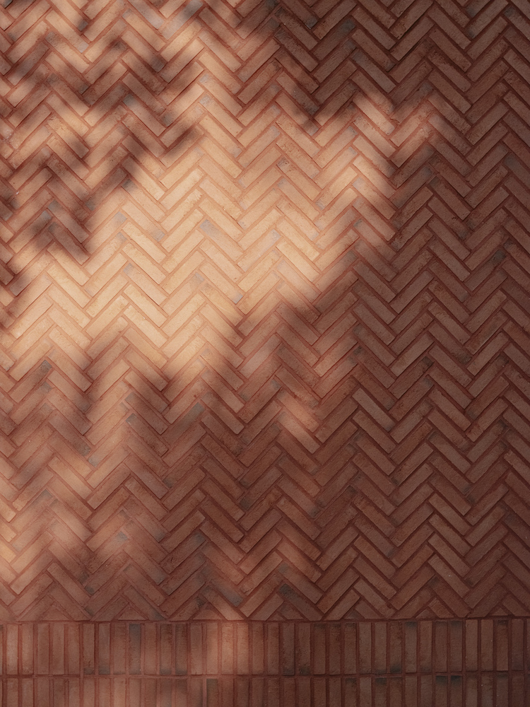 Herringbone terracotta brick wall with soft light casting diagonal shadows across the surface