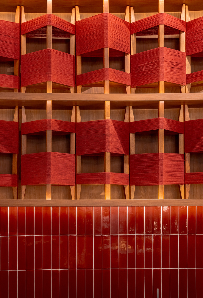 Facade detail with woven red textile panels wrapped around timber frames above a red tiled base