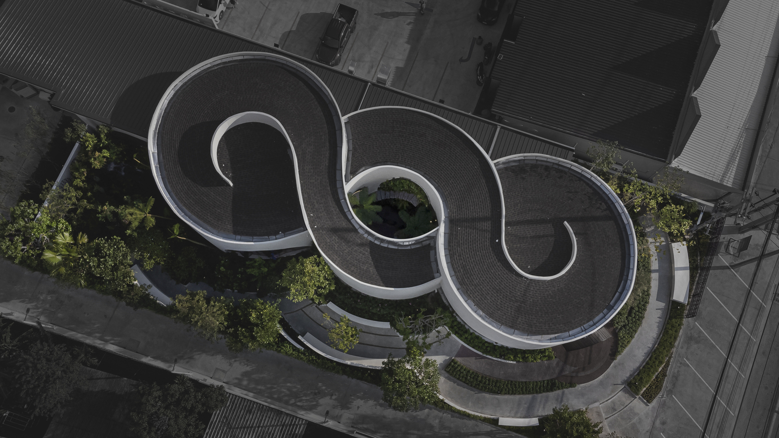 Aerial view of three spiral-shaped roof volumes with planted courtyards and paving between neighboring buildings
