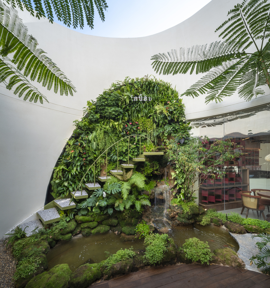 Courtyard with circular pond and planted green wall beneath curved white walls and overhanging fern fronds