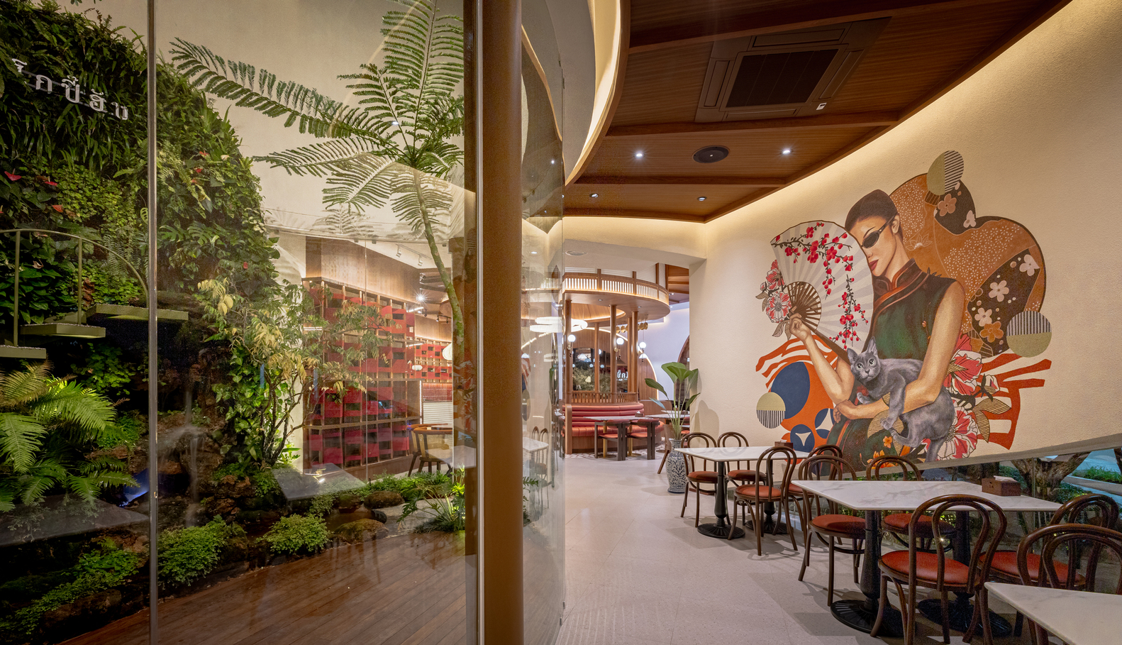 Dining space with glass-enclosed planted courtyard and wall mural of figures in traditional dress