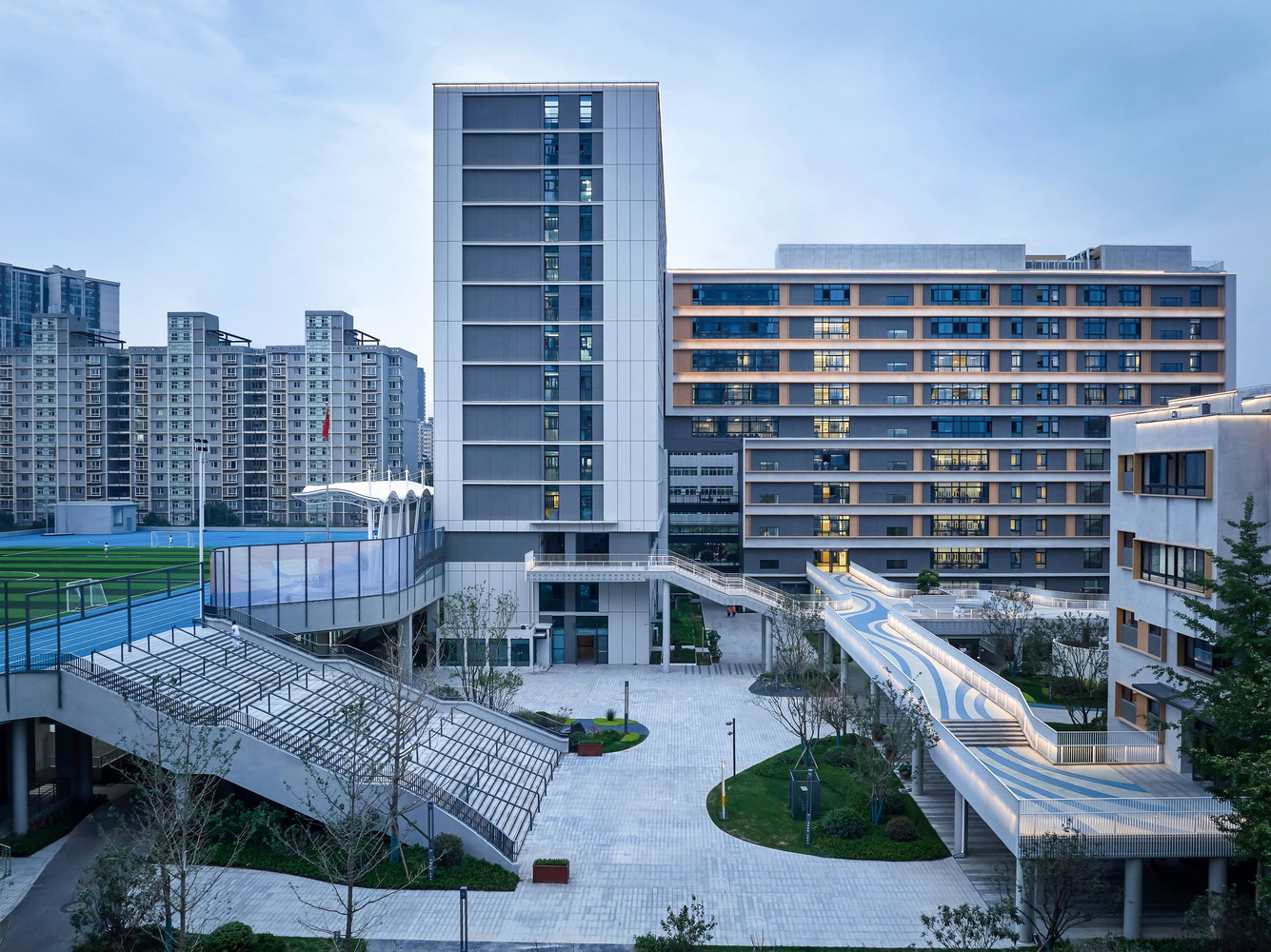 Elevated view of the courtyard with a serpentine pedestrian bridge connecting residential towers at dusk