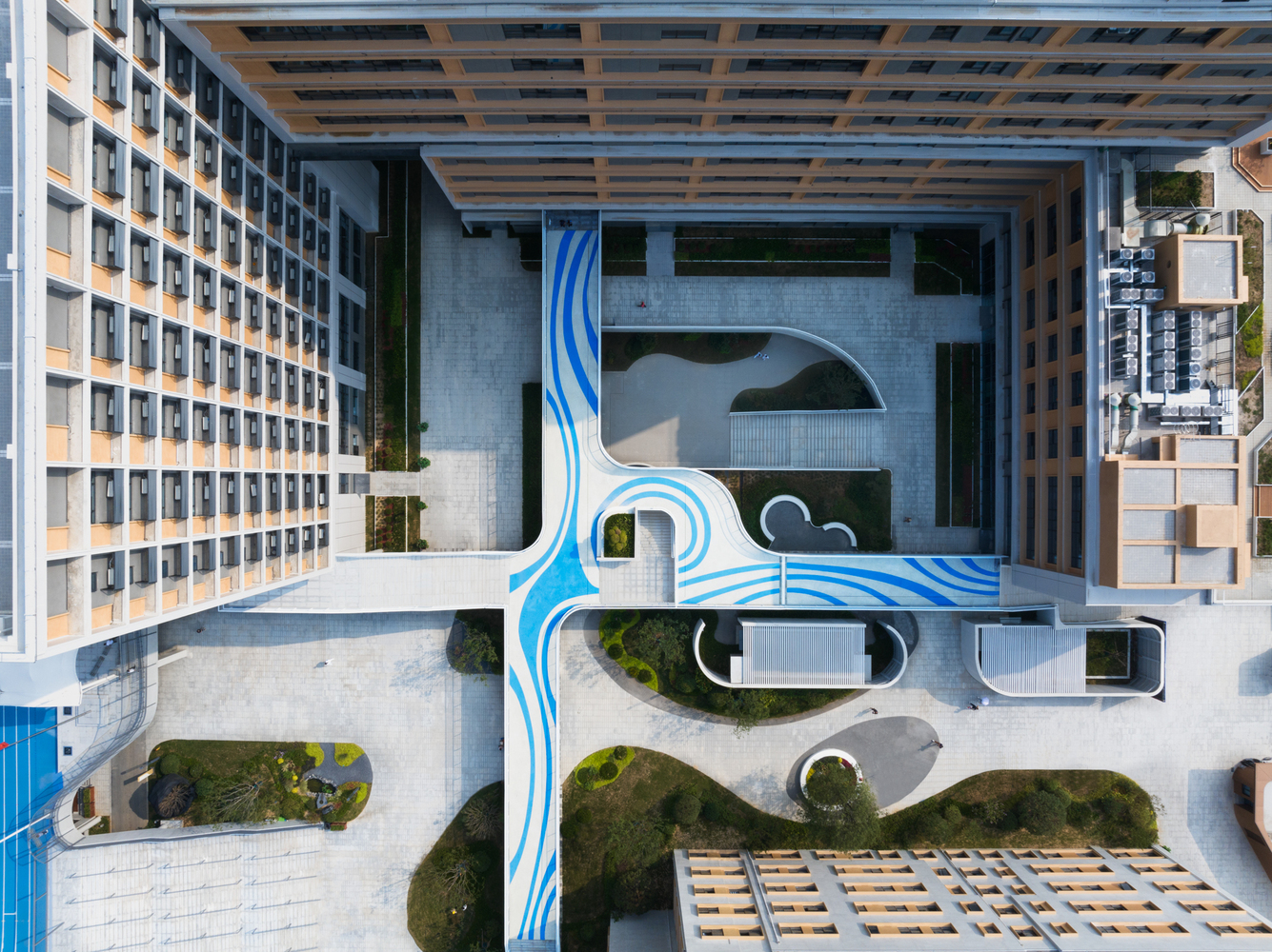 Aerial view of the courtyard showing blue painted pedestrian pathways winding between planted beds and buildings