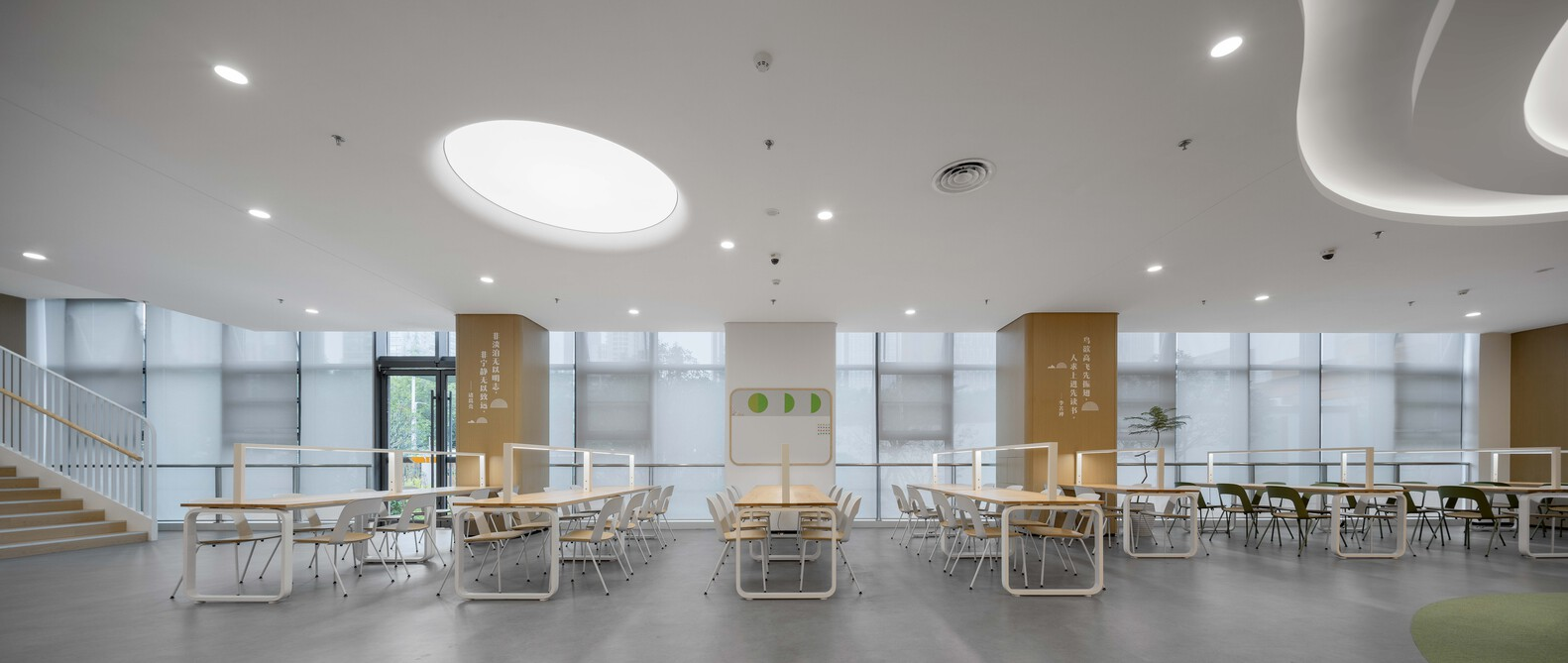 Cafeteria space with circular skylights, translucent wall panels and rows of tables and chairs on grey flooring