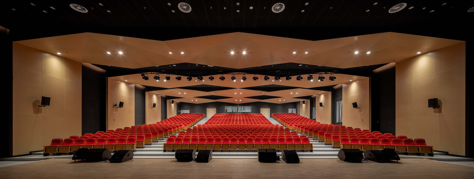 Auditorium interior with red upholstered seats, curved ceiling panels, and recessed lighting