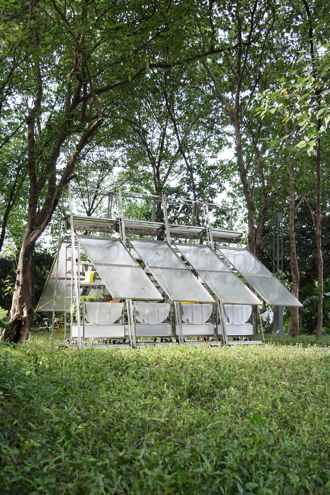 Long view of the portable greenhouse structure with tilted roof panels in a clearing among trees