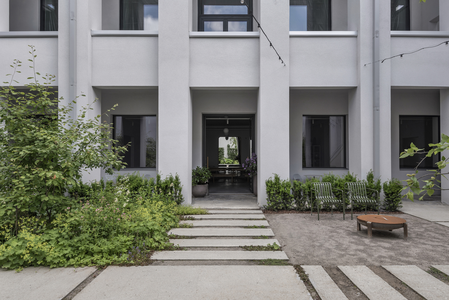 Courtyard entry with white concrete facade, deep recessed portals and planted beds flanking stone paving strips
