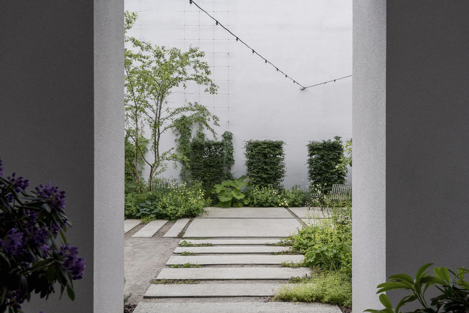 View through portal to a planted courtyard garden with cable trellis and white stucco walls