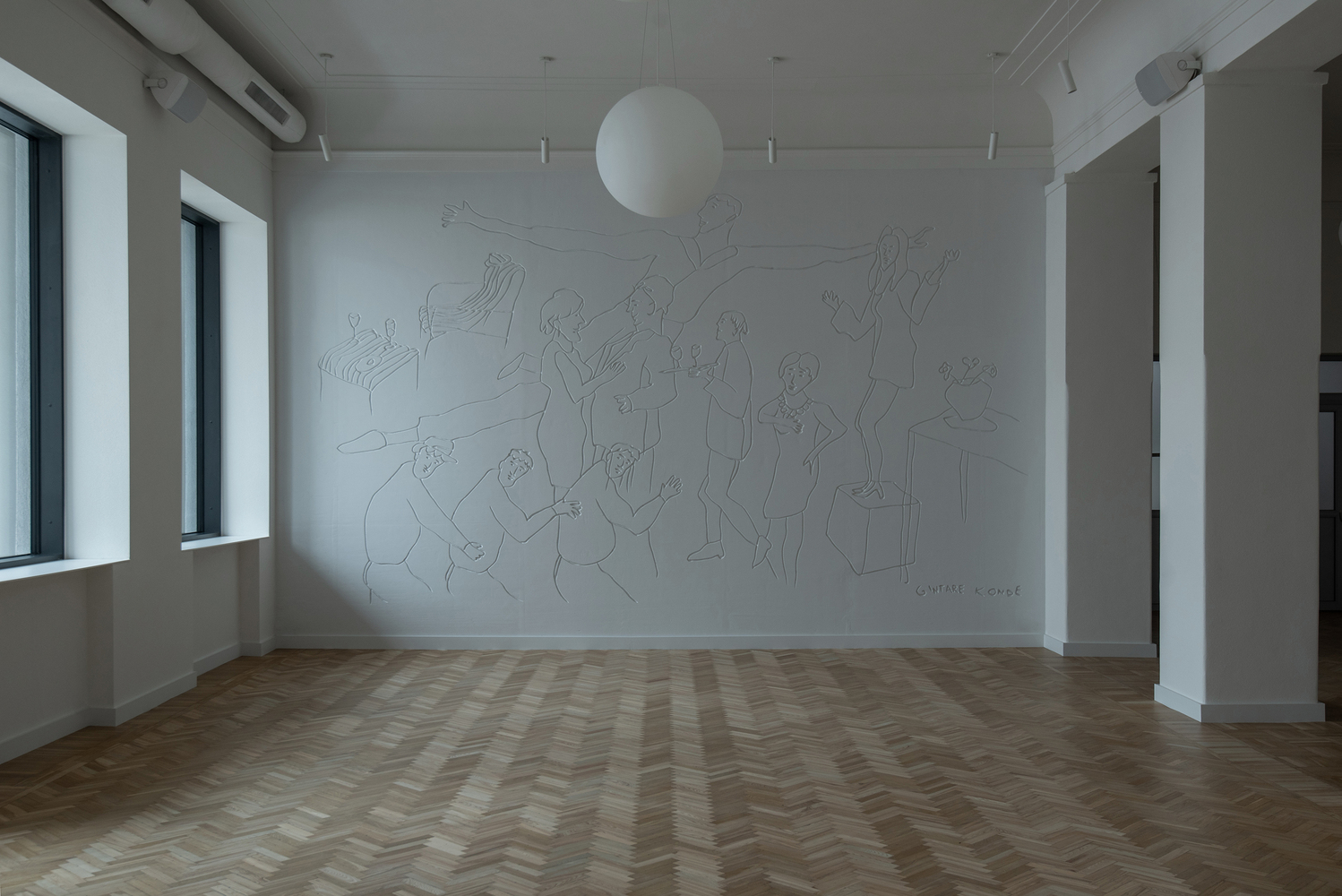 Empty room with herringbone oak floor, white walls with line mural and sphere pendant fixture