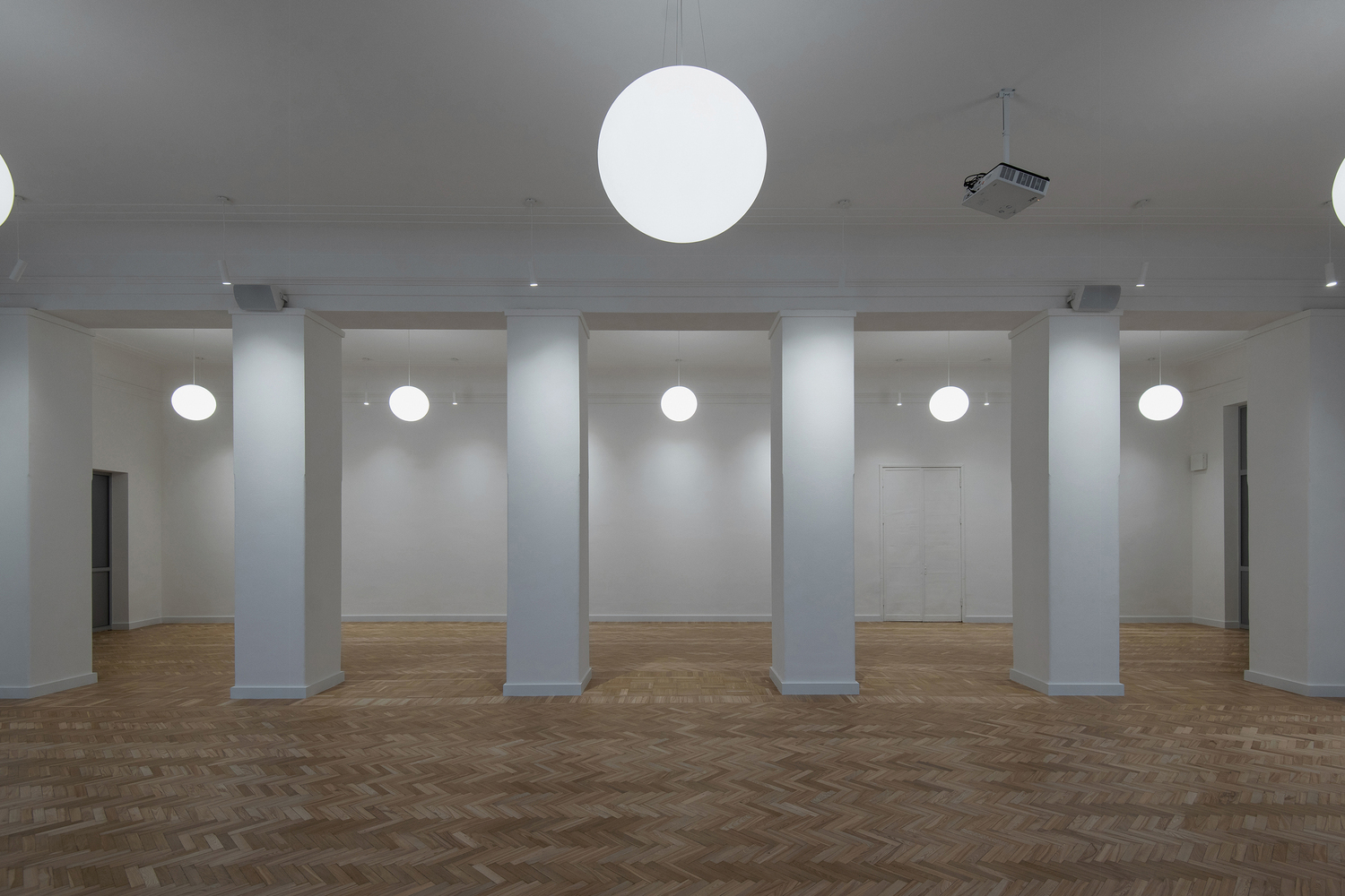 Interior room with herringbone oak flooring, white columns and sphere pendant lights suspended from the ceiling
