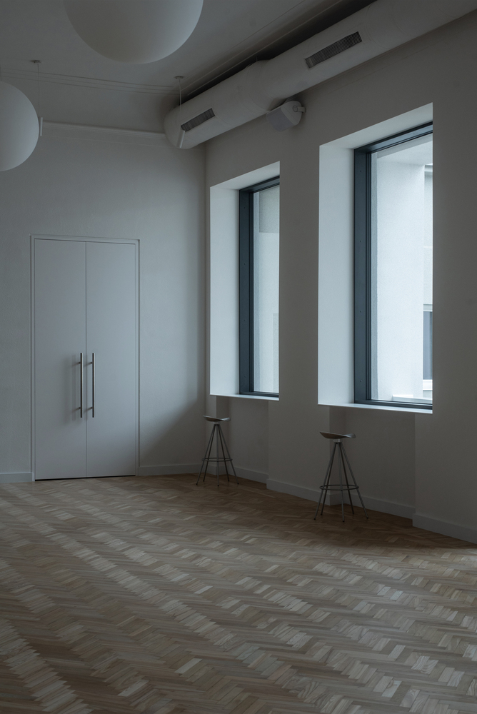 Corner room with two deep-set windows, herringbone oak flooring and two tripod stools beneath the openings