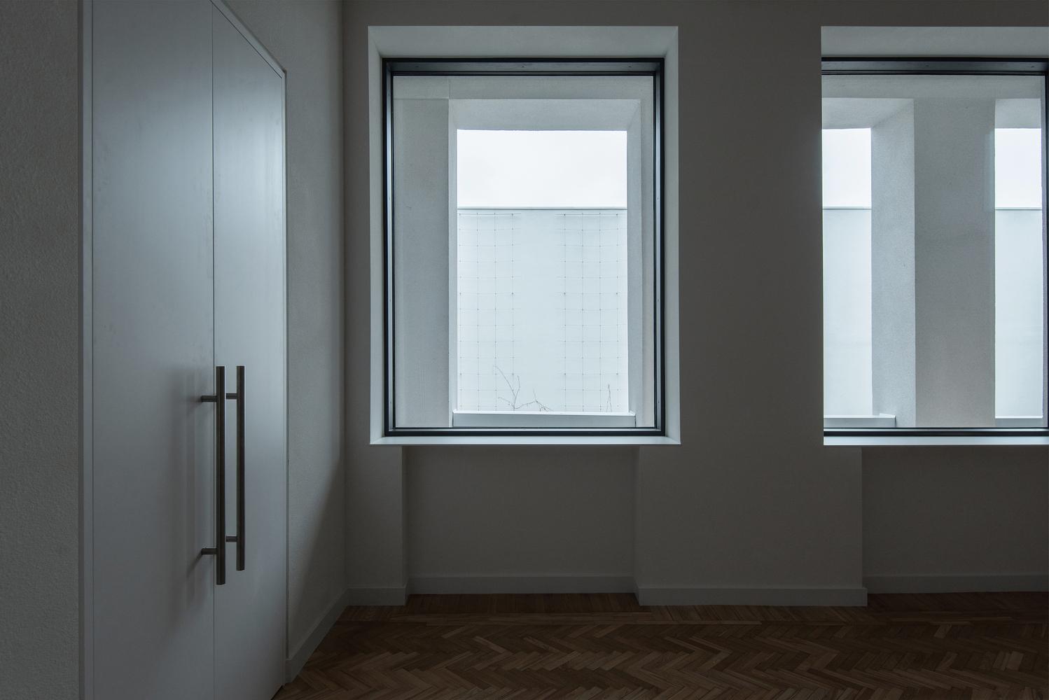 Deep window recess with dark metal frame looking onto a white tiled wall under overcast sky