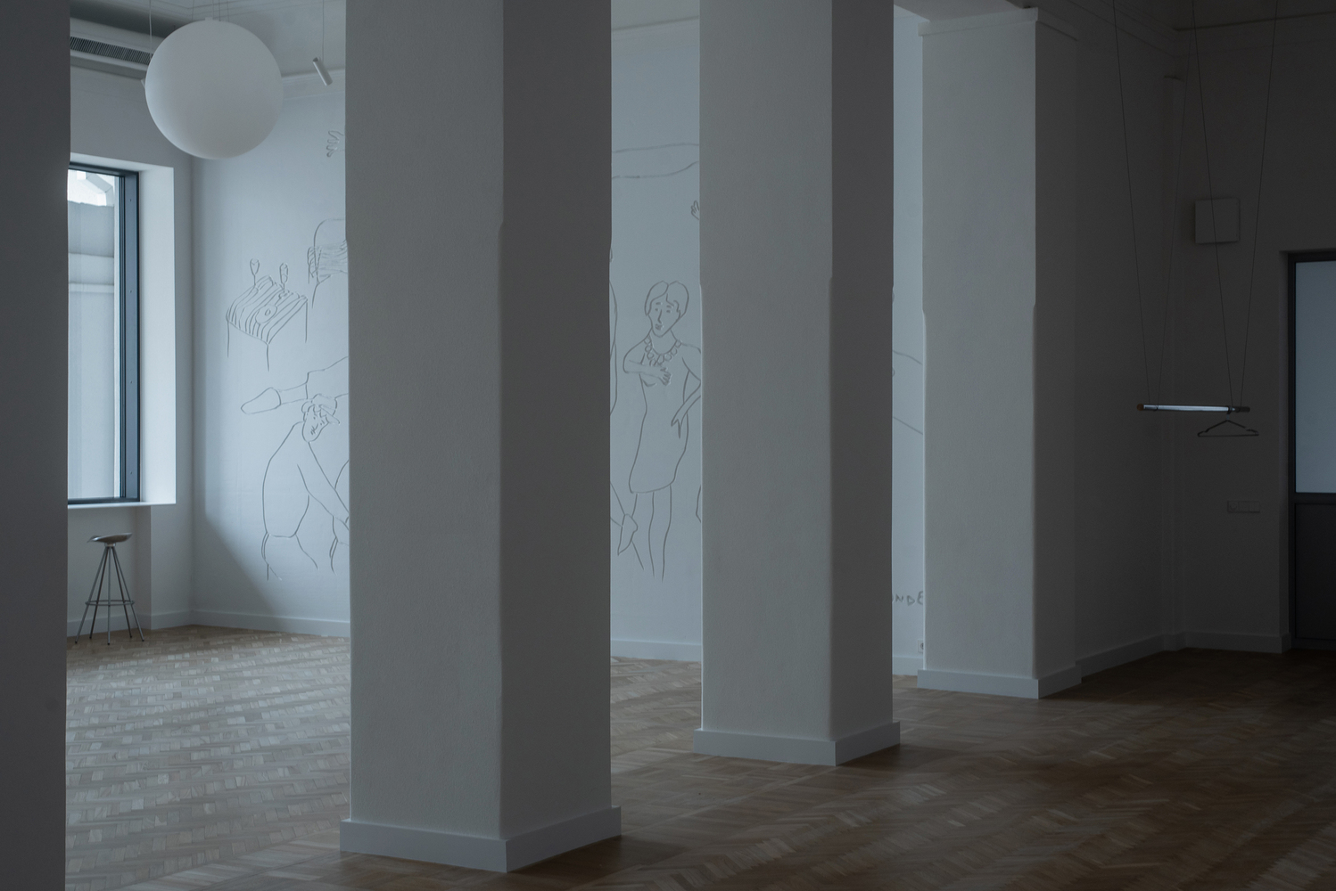 View through white columns showing parquet flooring and line drawings on the far wall
