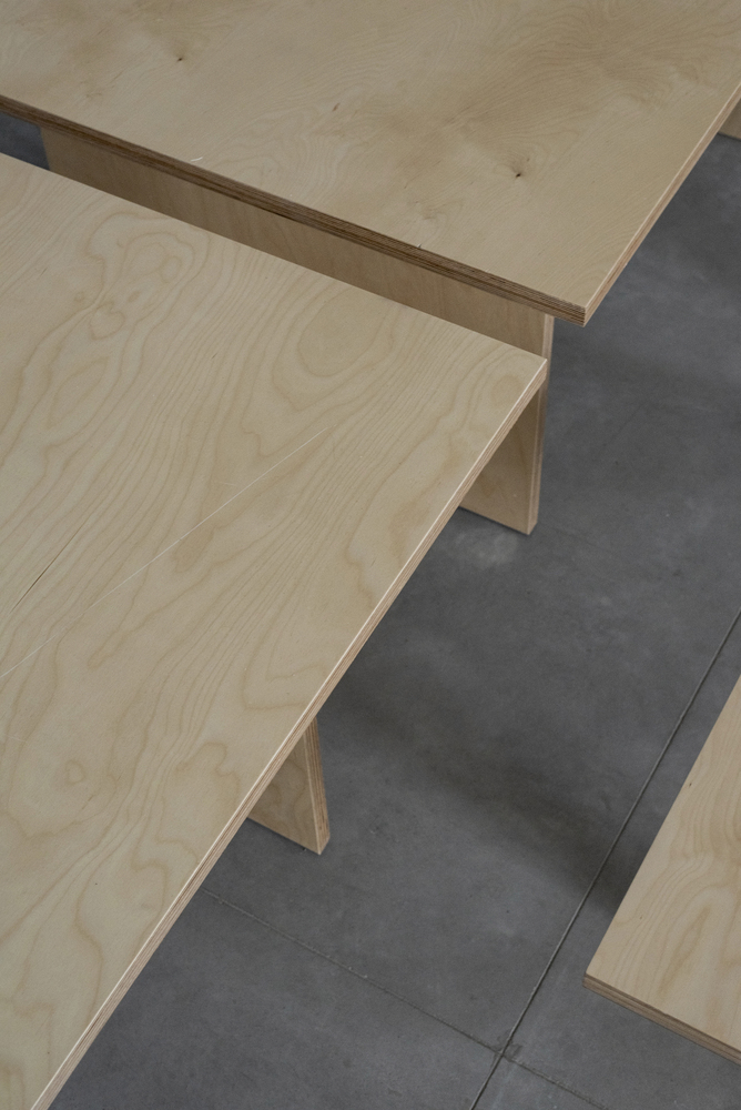 Detail of plywood benches with exposed edges meeting at a dark tiled floor