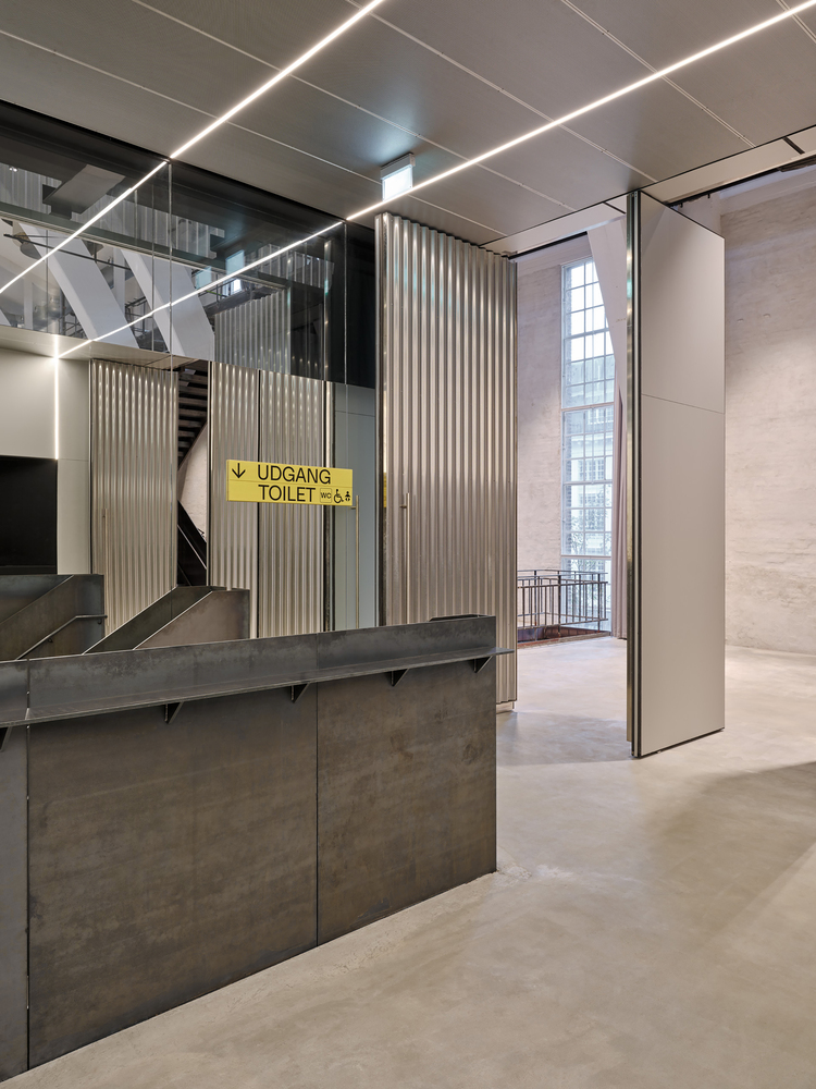 Foyer with stone-clad reception desk below linear ceiling lights and a yellow wayfinding sign