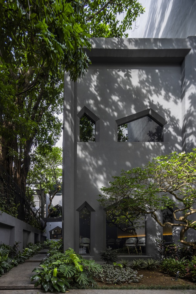 Textured concrete tower with peaked openings framed by dappled shadows from surrounding trees