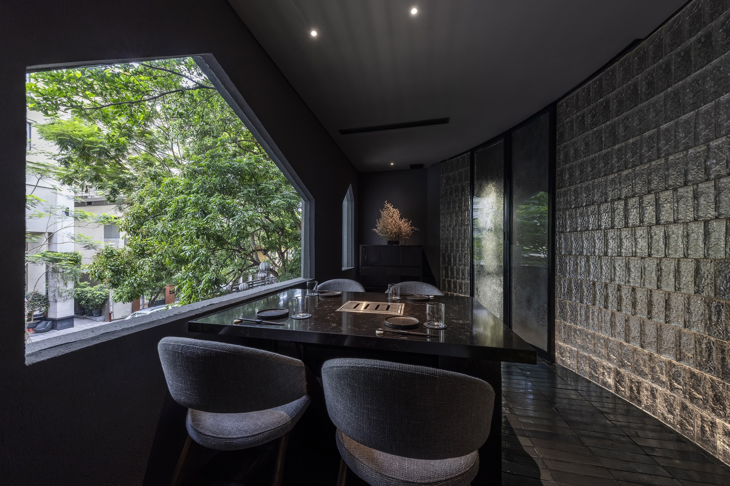 Interior dining space with angled window overlooking garden and decorative block wall illuminated by spotlights