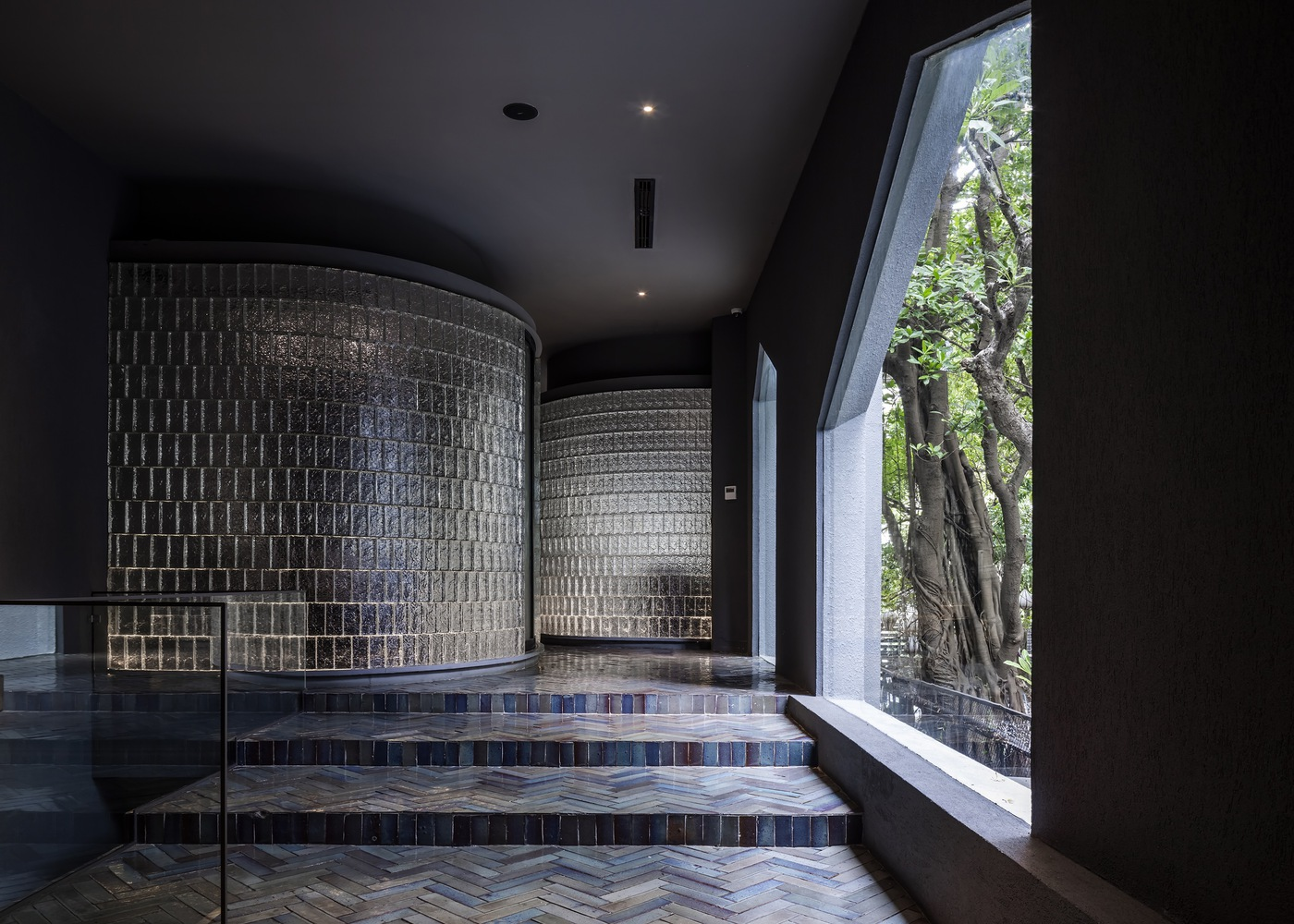 Curved patterned block walls flanking herringbone tile steps beneath a sloped black ceiling