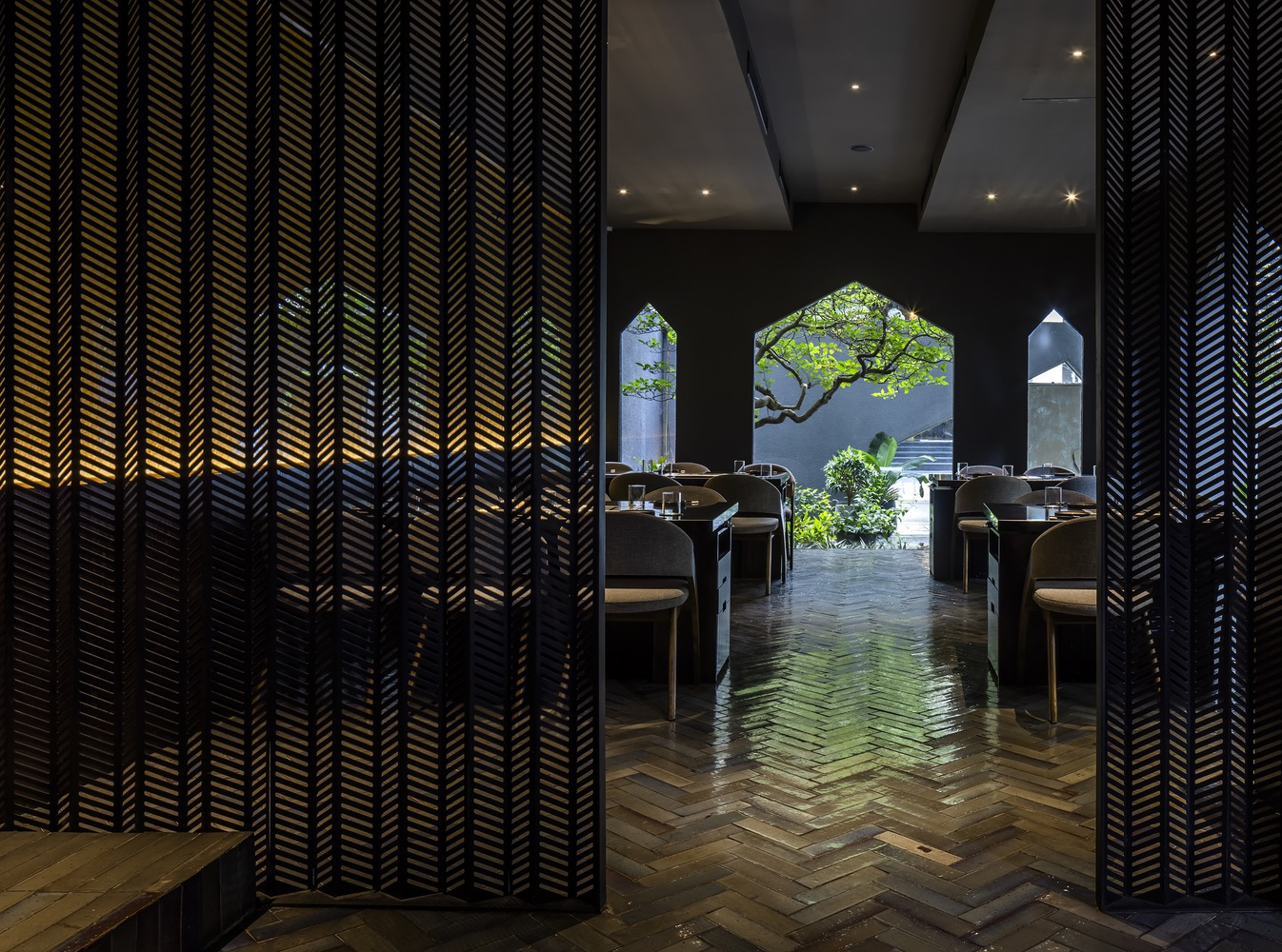 Herringbone timber floor between chevron-patterned screens framing house-shaped openings to garden
