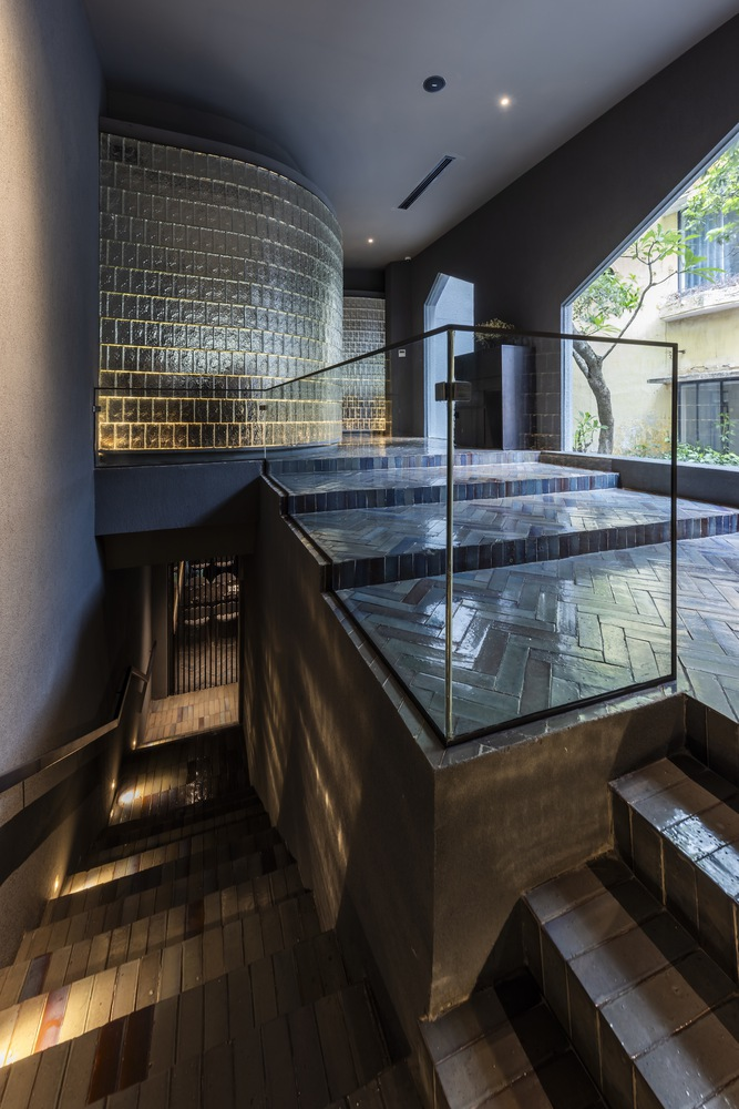 Multi-level interior with curved glass block wall and tiled staircase under glazed roof