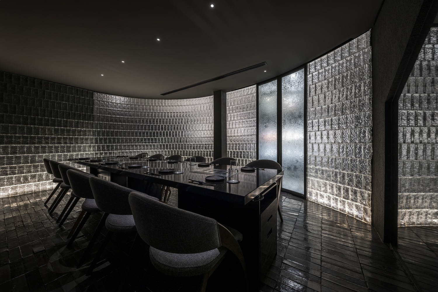 Dining room with curved glass block wall and dark timber floor beneath recessed ceiling
