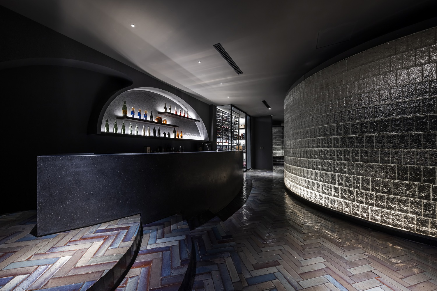 Bar area with curved glass block wall, herringbone wood flooring, and arched bottle display alcove