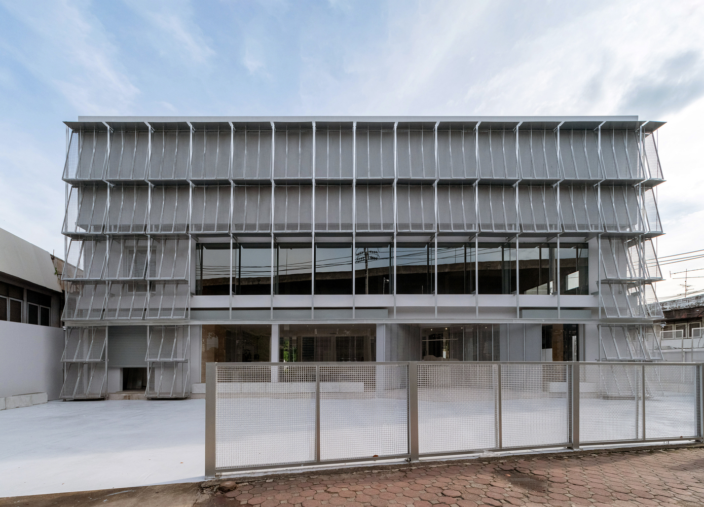 Front facade with perforated metal shutters and mesh gate under a cloudy sky
