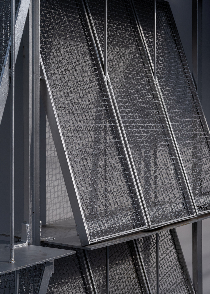 Close-up of hinged wire mesh solar screen panels framed in steel with diagonal bracing