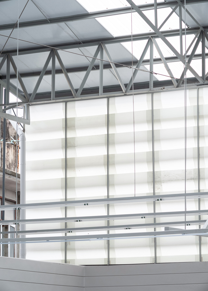 Interior view of exposed steel trusses above translucent polycarbonate wall panels diffusing daylight