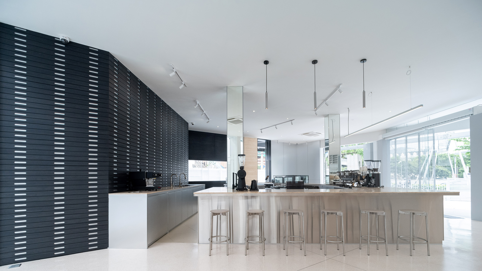 Long timber counter with bar stools facing black perforated wall beneath track lighting