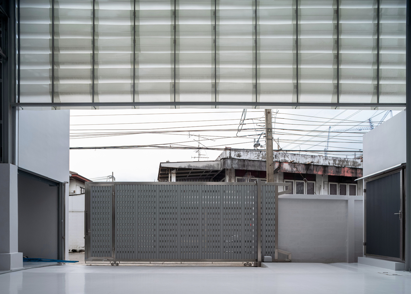 Perforated metal sliding gate framing view of weathered concrete structure and utility wires beyond