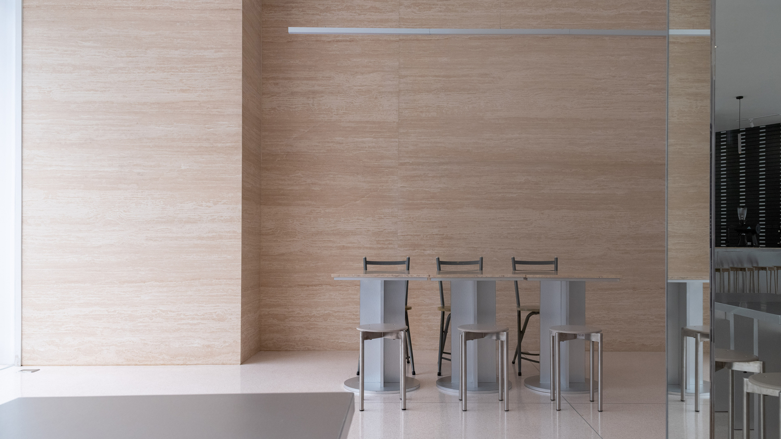 Metal bar stools arranged against pale wood grain wall panels with recessed glass door