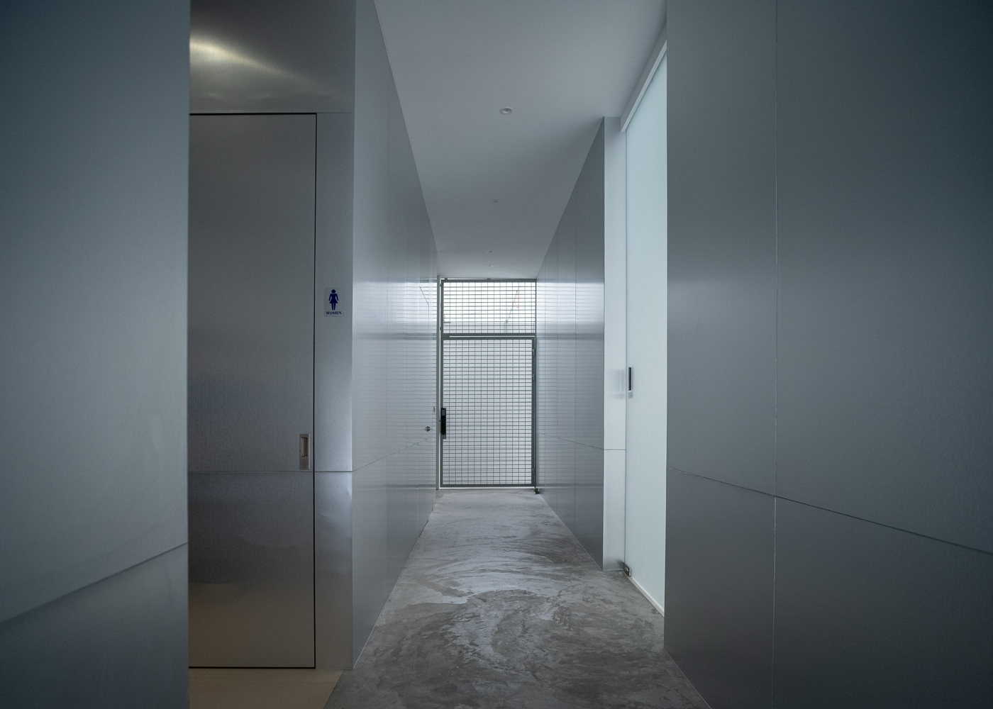 White tiled corridor leading to wire mesh door under concealed linear ceiling light
