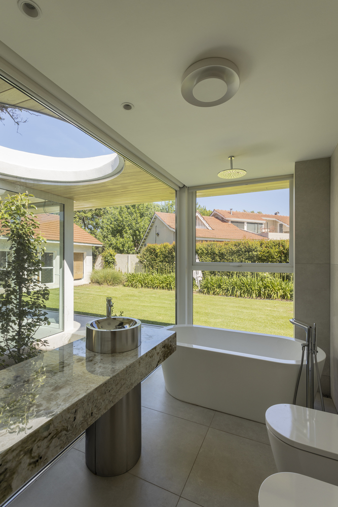 Bathroom with freestanding tub and circular skylight overlooking a lawn and neighboring houses