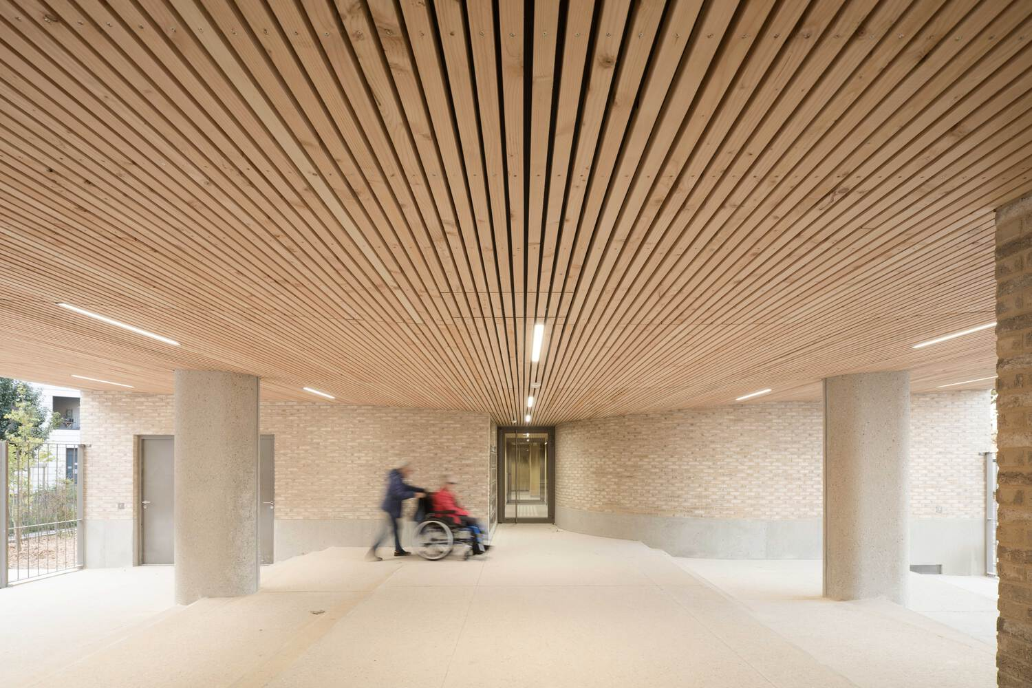 Ground floor entrance lobby with radiating timber slat ceiling and two figures moving through