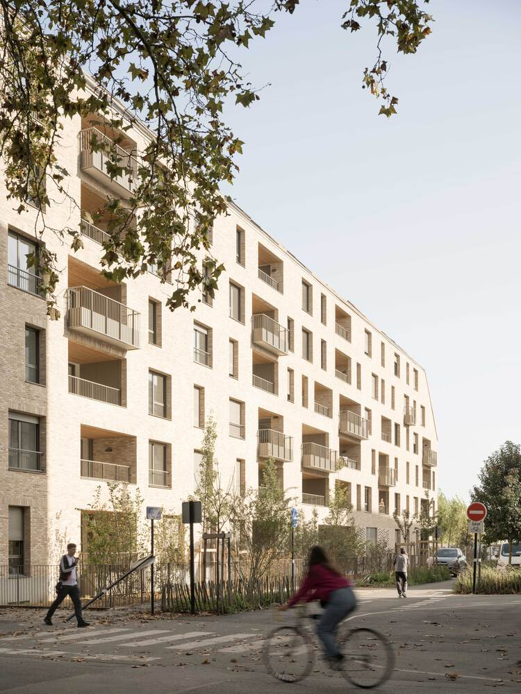 Street view of the residential facade with young trees and a cyclist passing by