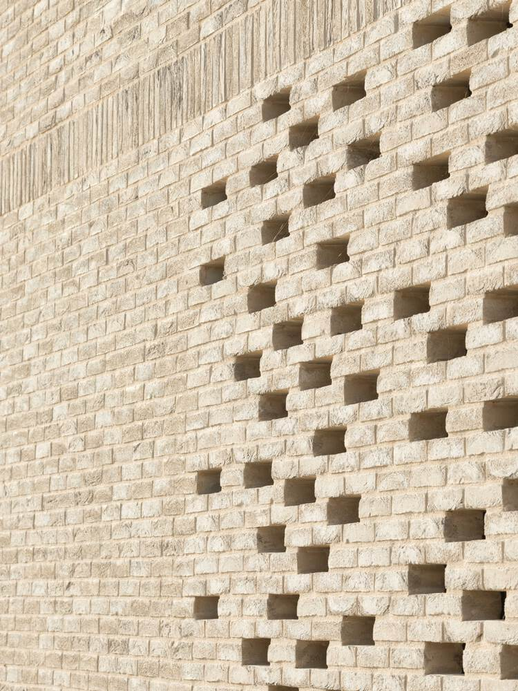 Close-up of pale brick wall with scattered square perforations casting shadows in sunlight