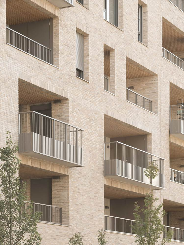 Staggered balconies with timber soffits and metal railings set into a pale brick facade with young trees