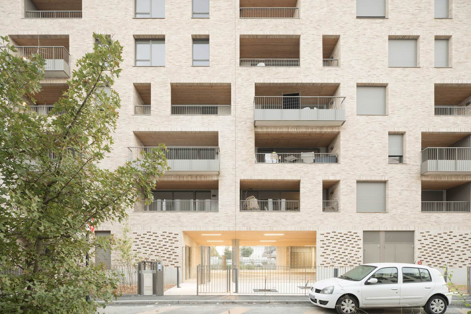 Ground-level entrance with perforated brick screen and recessed timber soffit beside a parked white car
