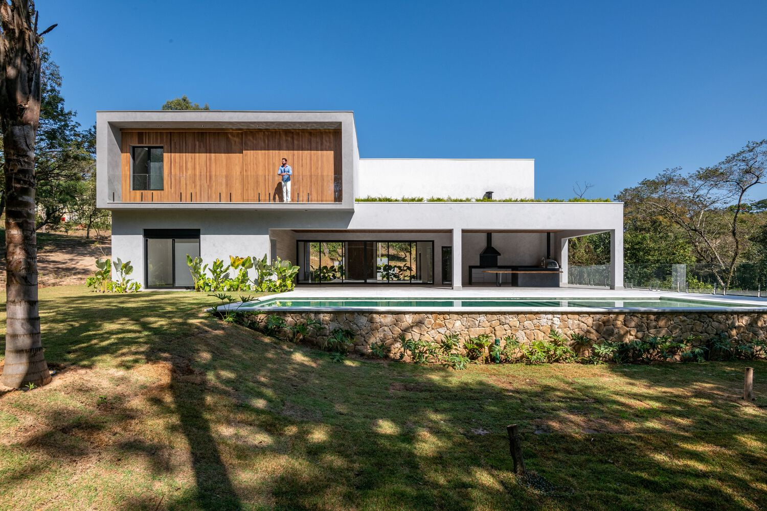 Rear elevation with white stucco volumes and timber cladding set into a sloping lawn with mature trees