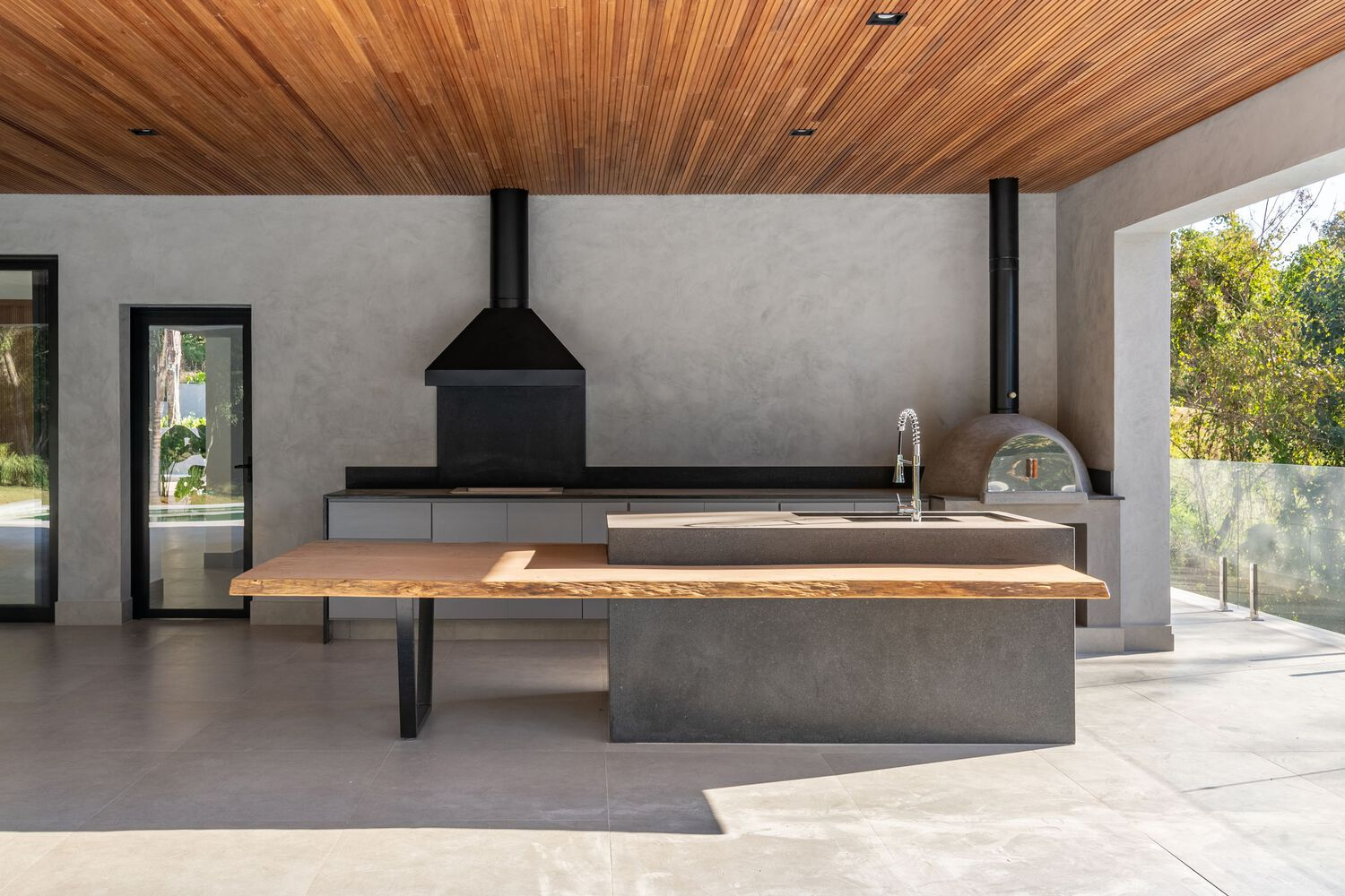 Outdoor kitchen island with timber slab counter, concrete base and wood slat ceiling overhead