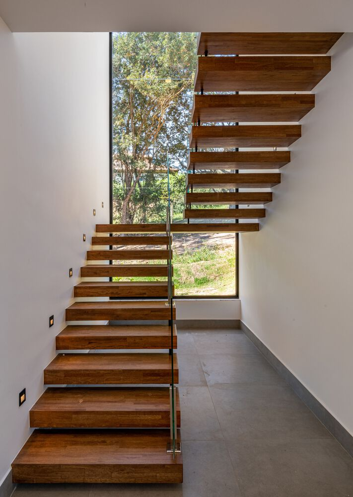 Cantilevered timber staircase with open risers beside a tall glazed corner framing garden views