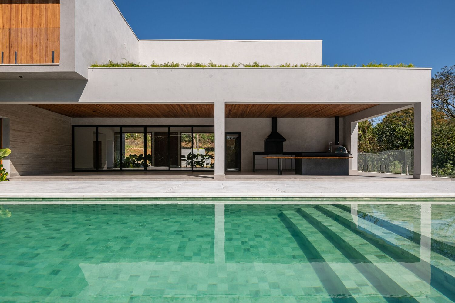 View across the swimming pool toward covered terrace with outdoor kitchen under timber soffit